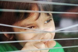 Portrait of an innocent small boy peeping through window with jalousie