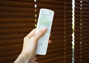 Hand holding remote control to open wooden blinds